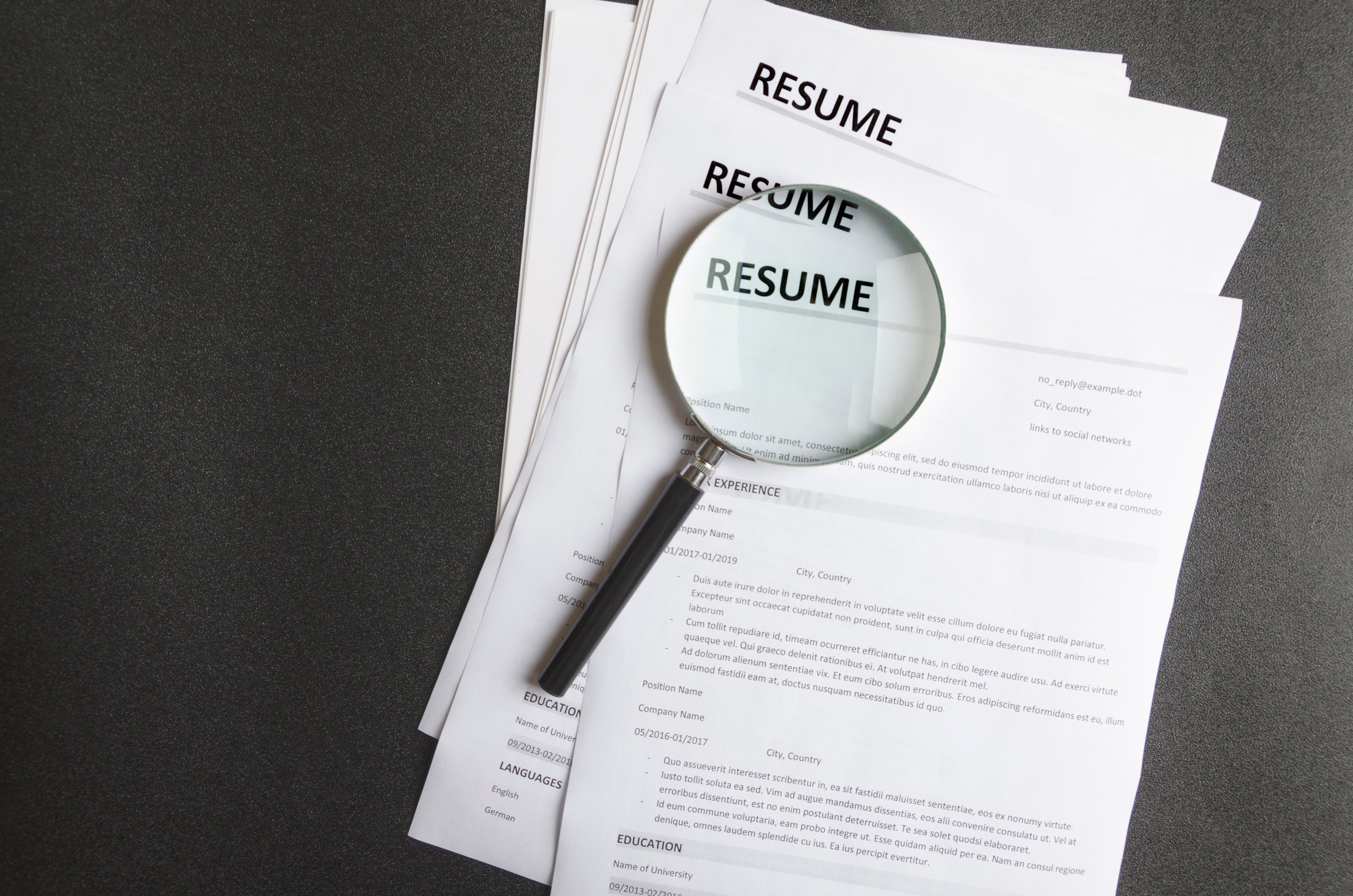 Top view of stack of resume files,magnifier on black surface.Concept of reviewing resume applictaions,searching for new employees